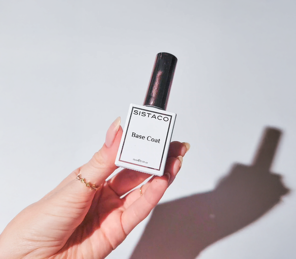 Hand holding a bottle of SISTACO Base Coat nail polish against a light background